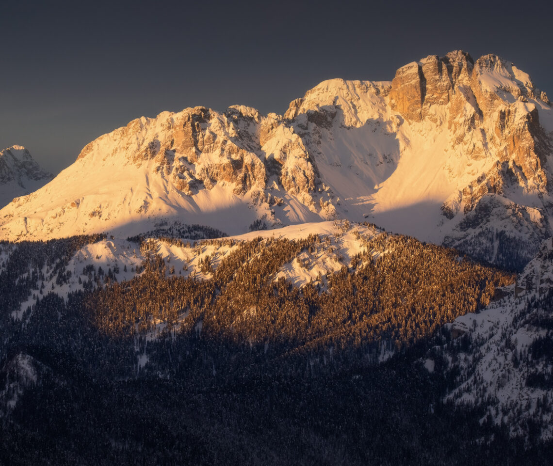 Il cielo plumbeo all’orizzonte risalta ancor di più la lucentezza di un’alba tanto attesa in uno scenario gelido. Alpi Carniche e Dolomiti, Italia.