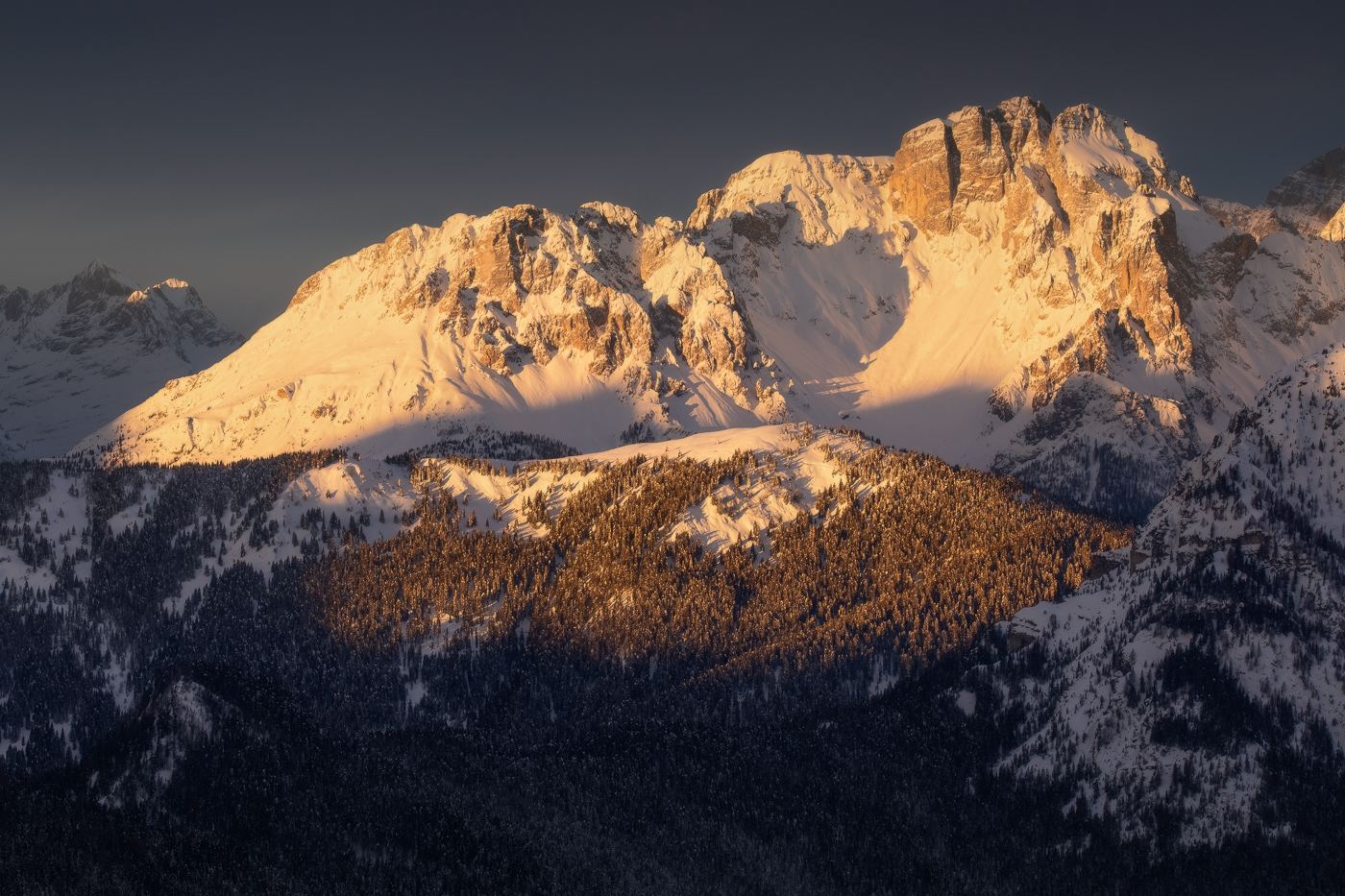 Il cielo plumbeo all’orizzonte risalta ancor di più la lucentezza di un’alba tanto attesa in uno scenario gelido. Alpi Carniche e Dolomiti, Italia.