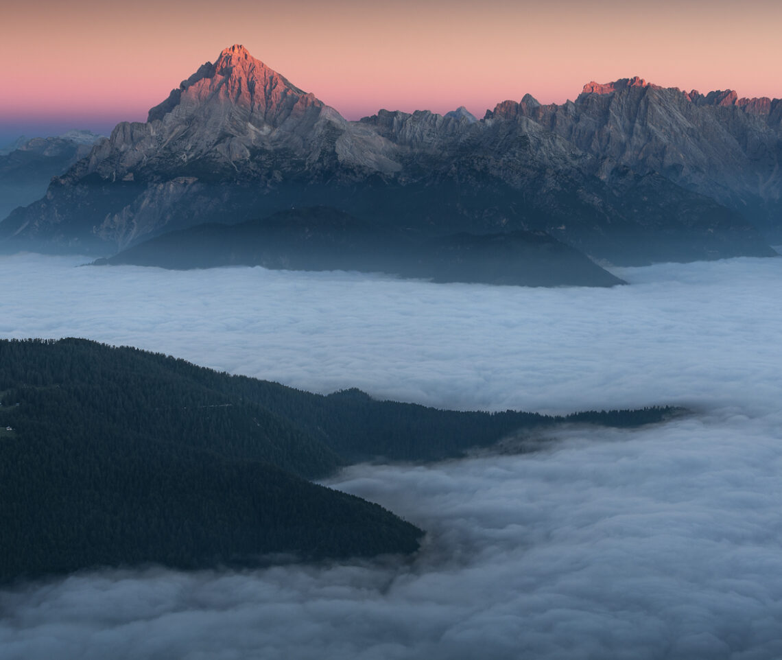 Mentre il Cadore giace ancora in un sonno profondo sotto uno spesso strato di nubi basse, la luce, quassù, è già all’opera: il paesaggio si infiamma. Dolomiti Cadorine e Gruppo delle Marmarole dalle Dolomiti Friulane, Italia.