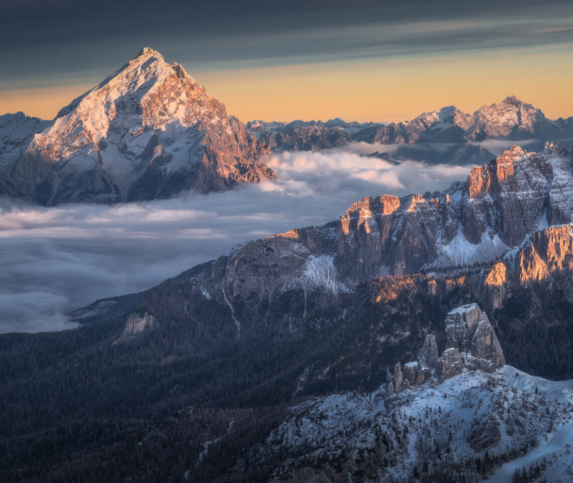 Estese e scure nubi alte danno risalto alle tonalità calde che accendono il Re delle Dolomiti, il monte Antelao. La Valle del Boite, invece, è già sommersa dall’oscurità. Dolomiti Ampezzane, Italia.