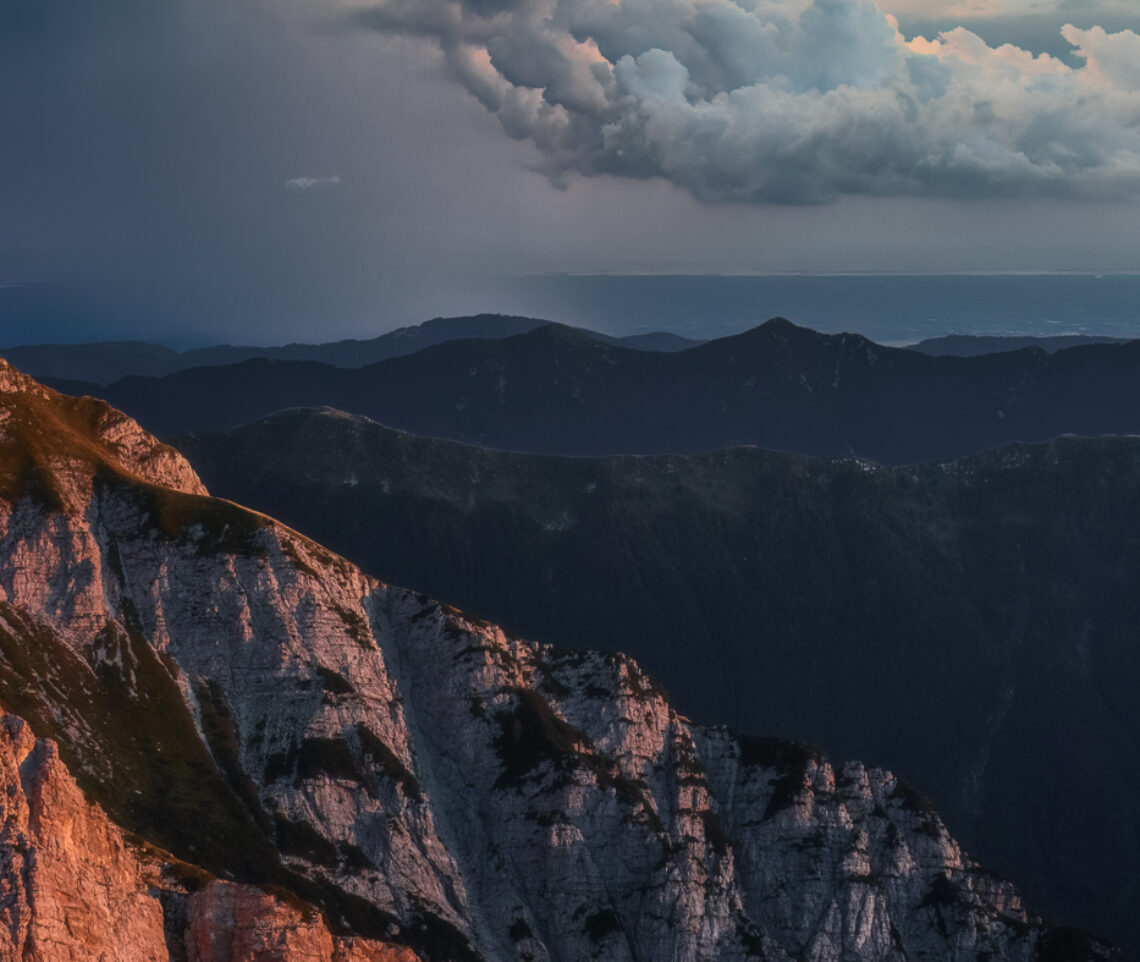 Fra le Alpi Giulie e il Mar Adriatico si frappone un improvviso temporale ammantato dell’oro del tramonto. Parco Naturale Prealpi Giulie, Italia.