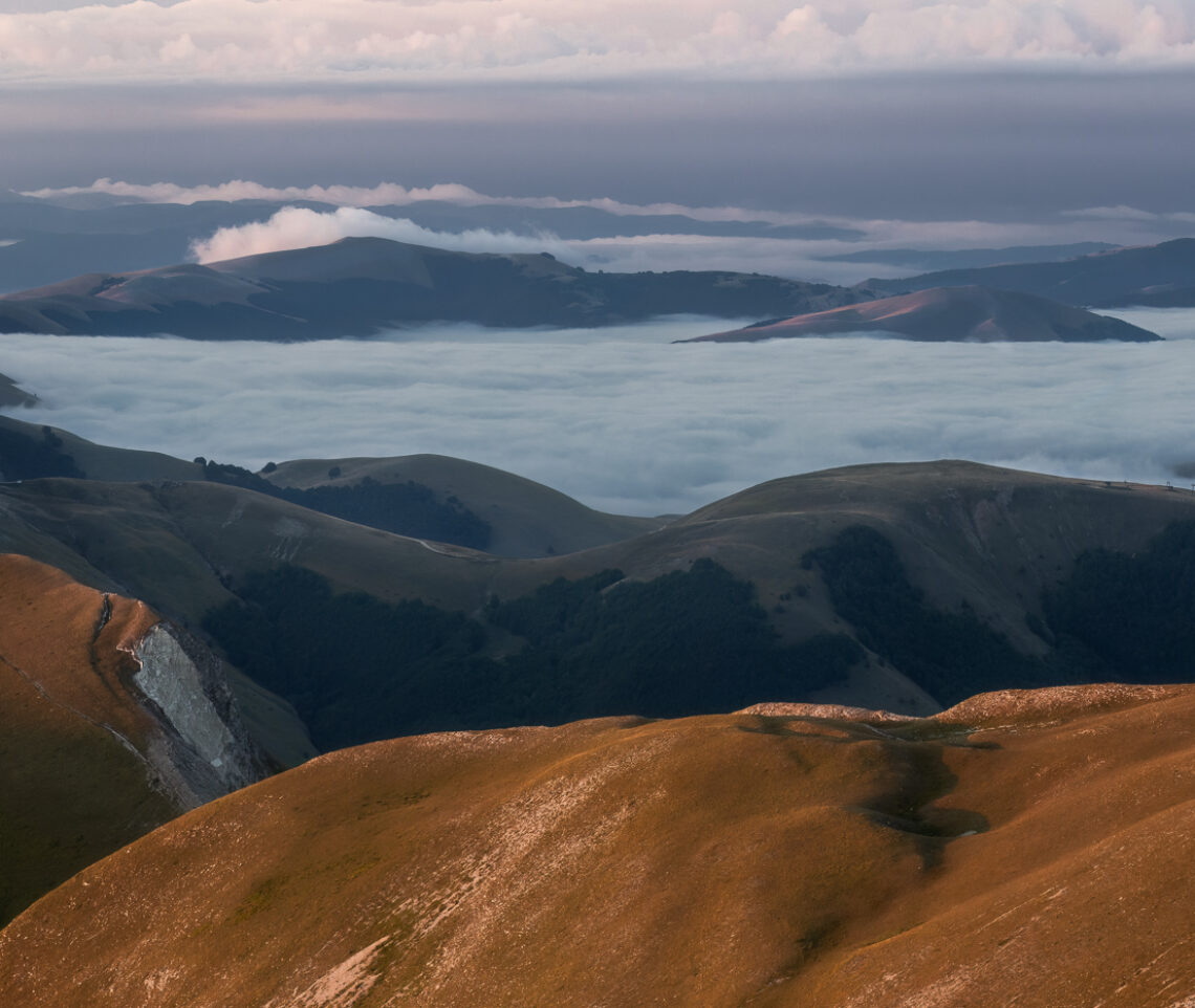 La piana di Castelluccio di Norcia è ancora immersa in un mare di nubi fra l’alba alle mie spalle e un temporale all’orizzonte. Parco Nazionale dei Monti Sibillini, Italia.