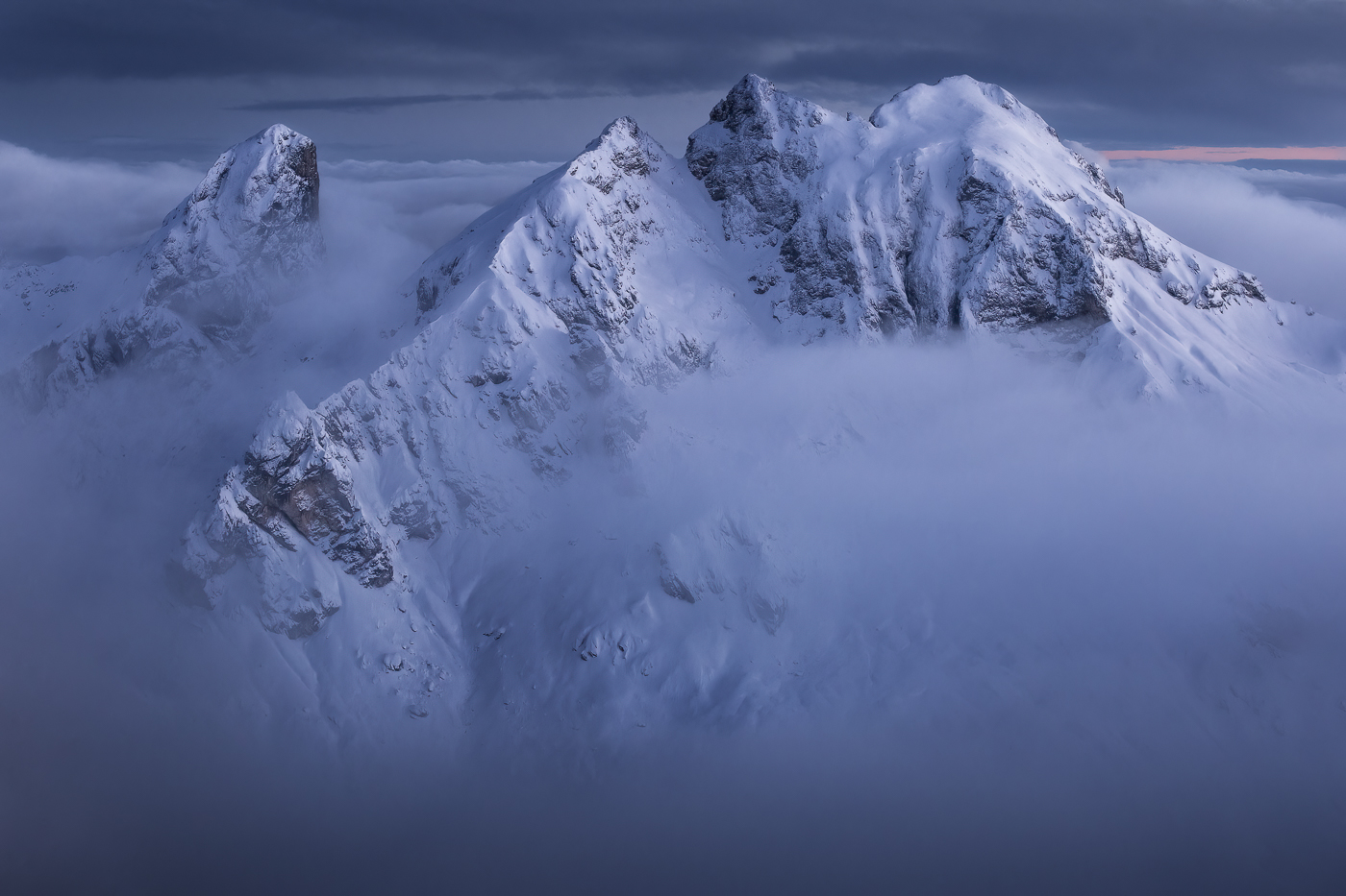 Cime sagomate dallo scenario invernale emergono da un mare di nubi per diventare anch’esse protagoniste dell’ora blu. Dolomiti Ampezzane, Italia.