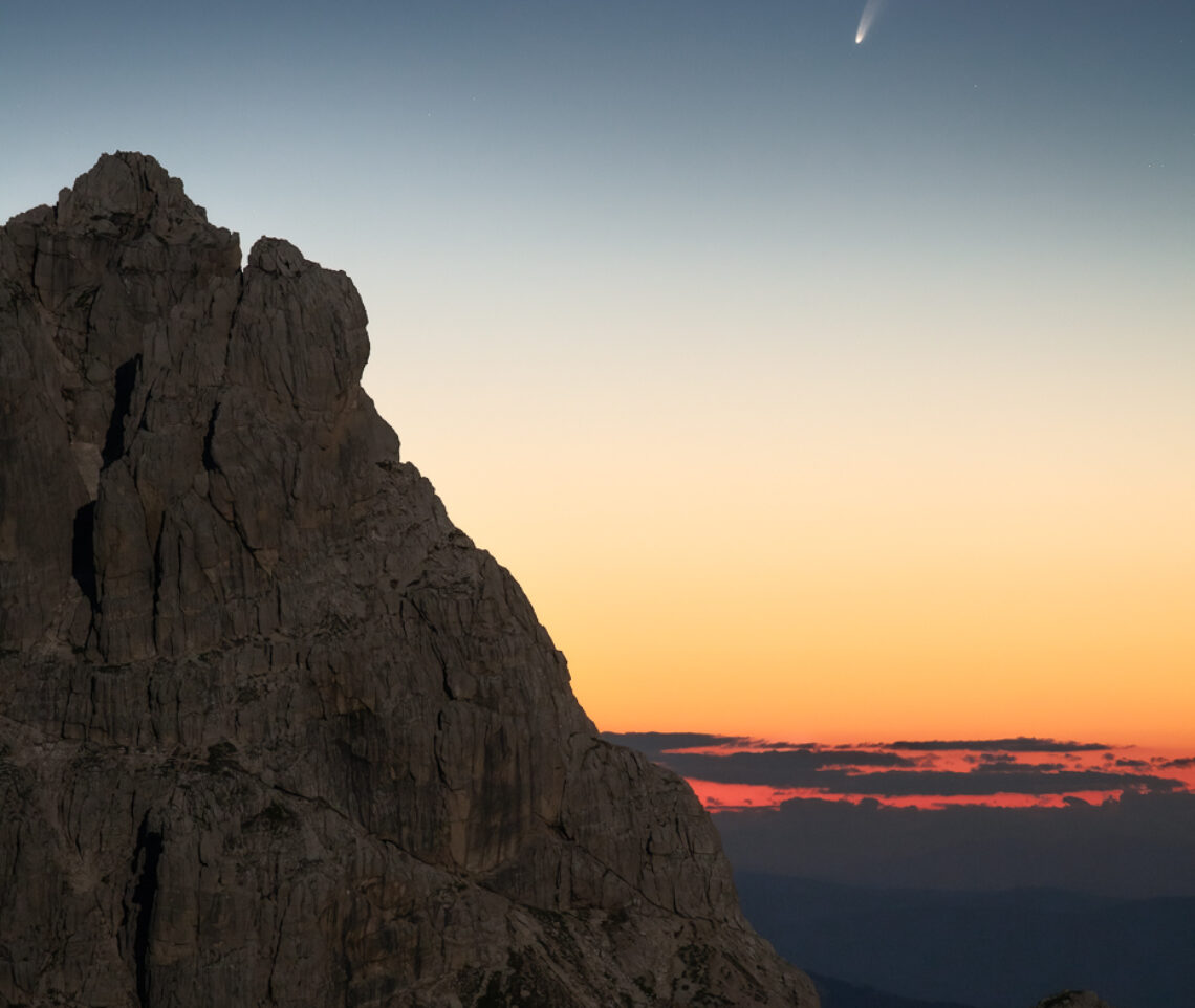 Flebile ma ancora accesa, resiste in cielo la cometa C/2020 F3 (NEOWISE) prima dell’alba, fra le guglie delle Alpi Giulie illuminate dalla Luna piena. Alpi Giulie, Italia.