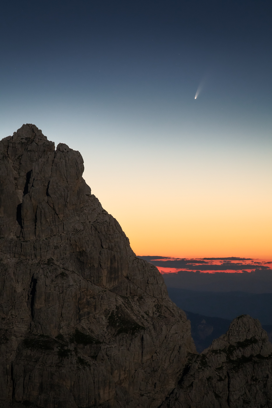 Flebile ma ancora accesa, resiste in cielo la cometa C/2020 F3 (NEOWISE) prima dell’alba, fra le guglie delle Alpi Giulie illuminate dalla Luna piena. Alpi Giulie, Italia.