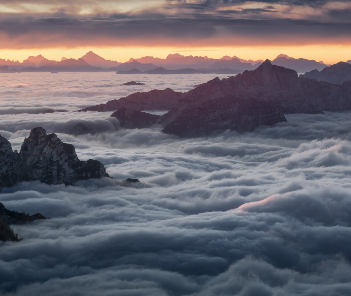 Lampi di fuoco squarciano il cielo durante un tramonto autunnale sopra le nubi, dalle vette delle Alpi Giulie, Italia.