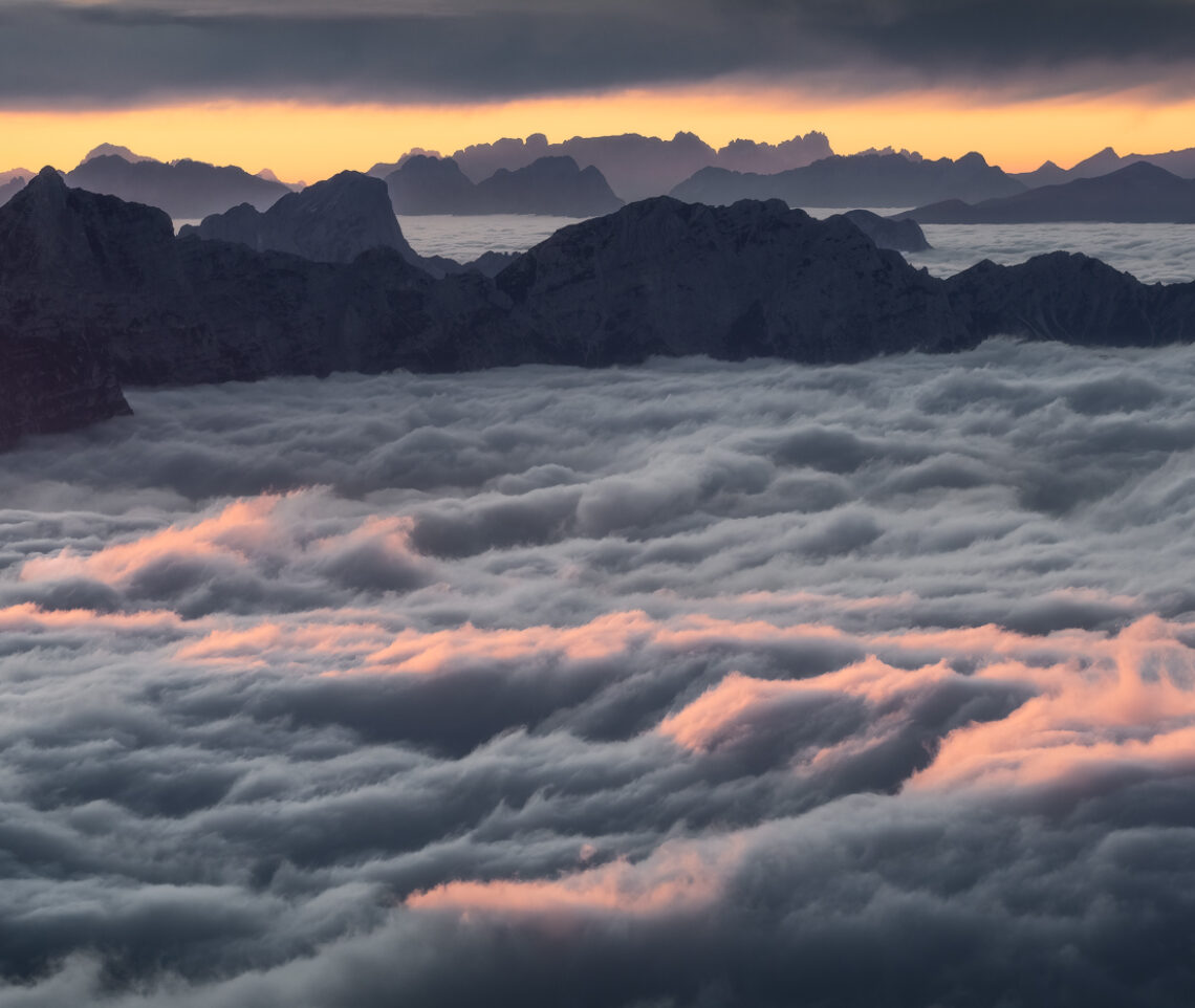 Terra! I profili delle Dolomiti di Sesto, sullo sfondo, risaltano, inconfondibili, navigando su questo mare di nuvole. Alpi Carniche e Dolomiti, Italia.