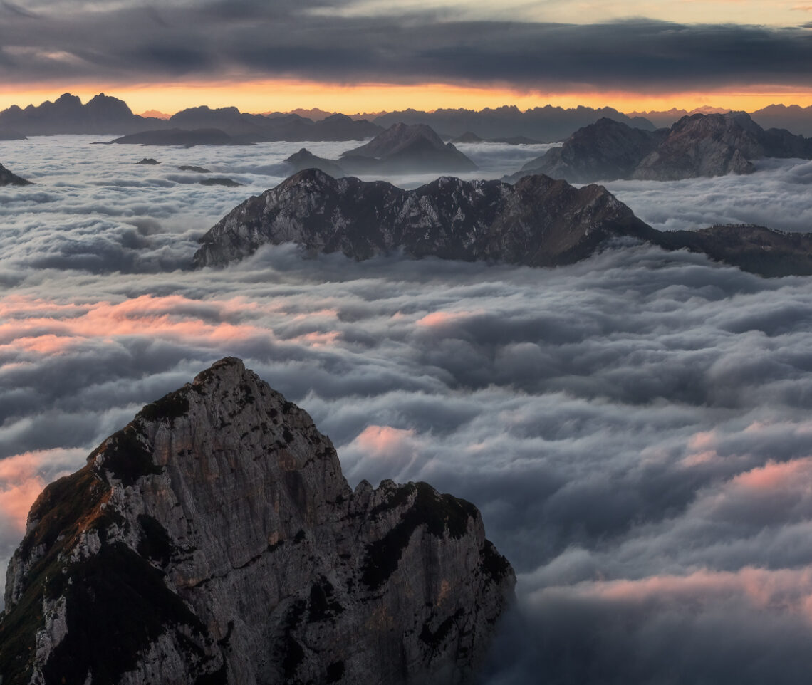 Fiamme inattese incendiano un mare di nubi attraverso il quale si stagliano isole rocciose a perdita d’occhio. Alpi Giulie e Carniche, Italia.