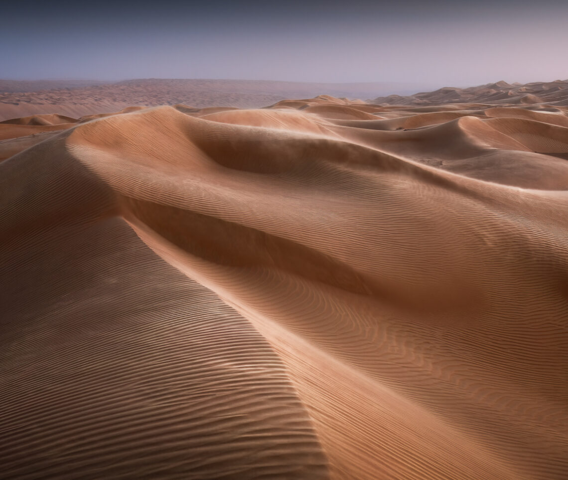 Al tramonto, un vento intenso spazza le creste delle dune, plasmandole, in un moto perpetuo. Oman.