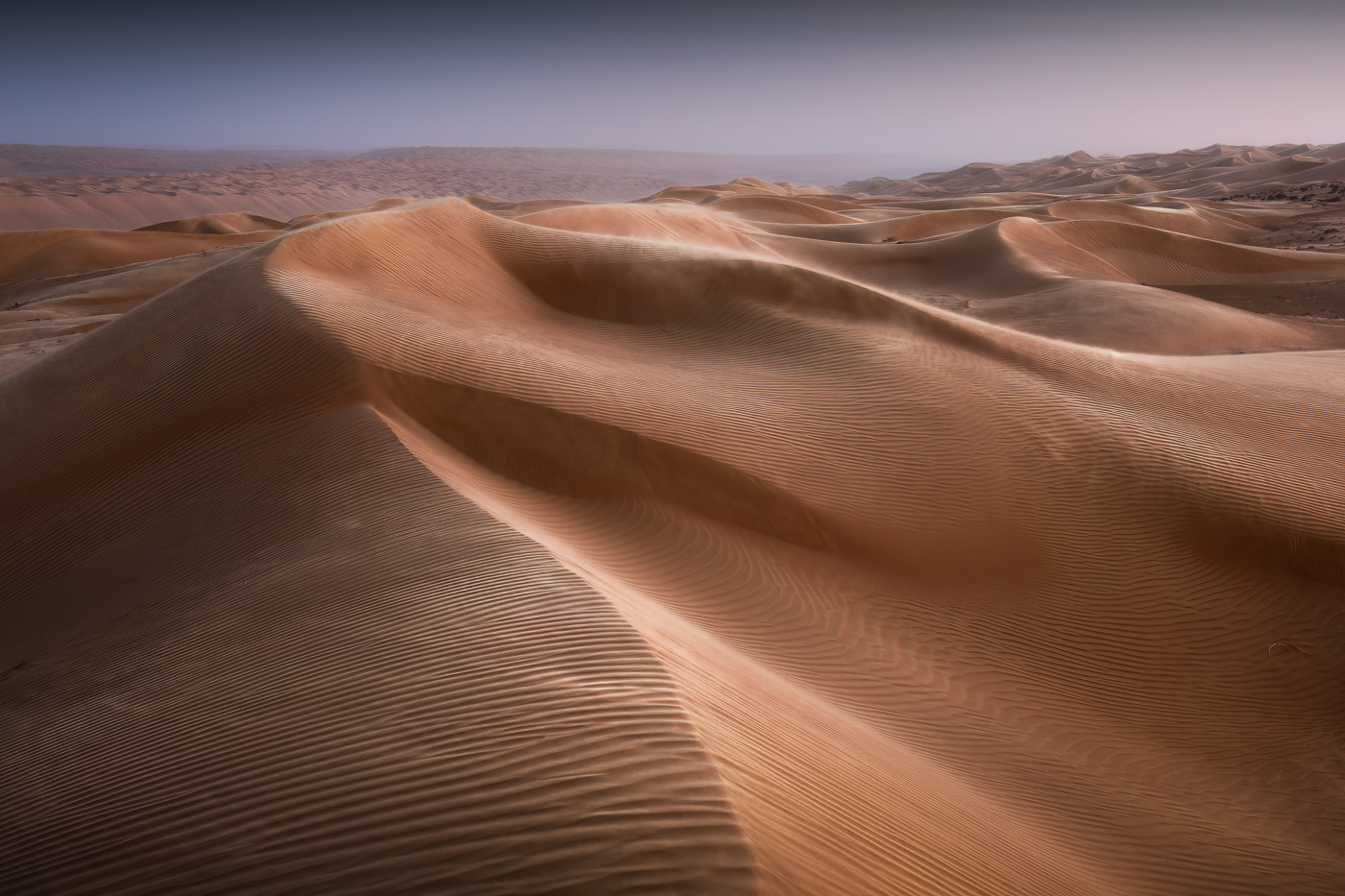 Al tramonto, un vento intenso spazza le creste delle dune, plasmandole, in un moto perpetuo. Oman.