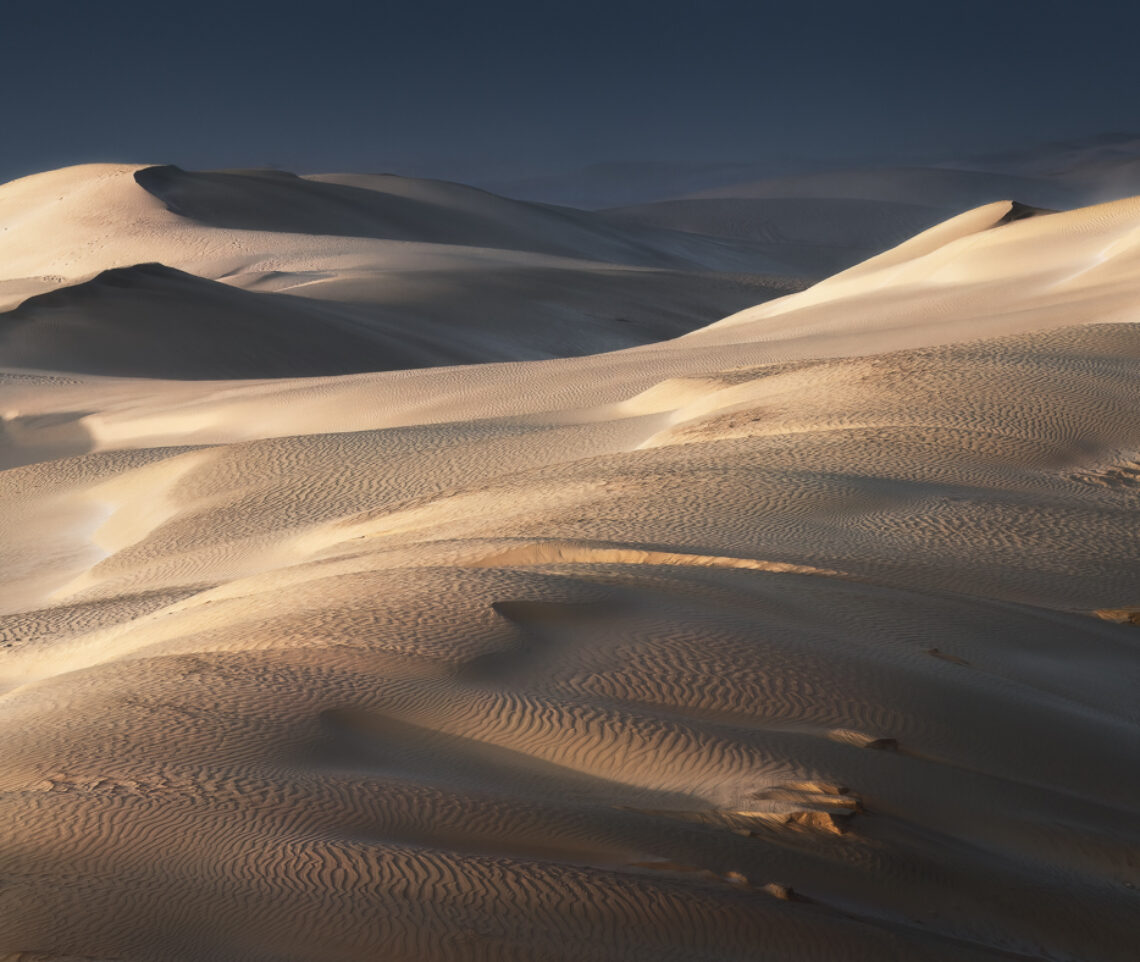 Le dune bianche del deserto splendono, illuminate dal Sole appena emerso dall’Oceano Indiano. Oman.