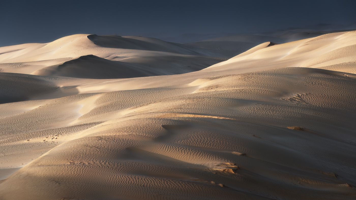 Le dune bianche del deserto splendono, illuminate dal Sole appena emerso dall’Oceano Indiano. Oman.