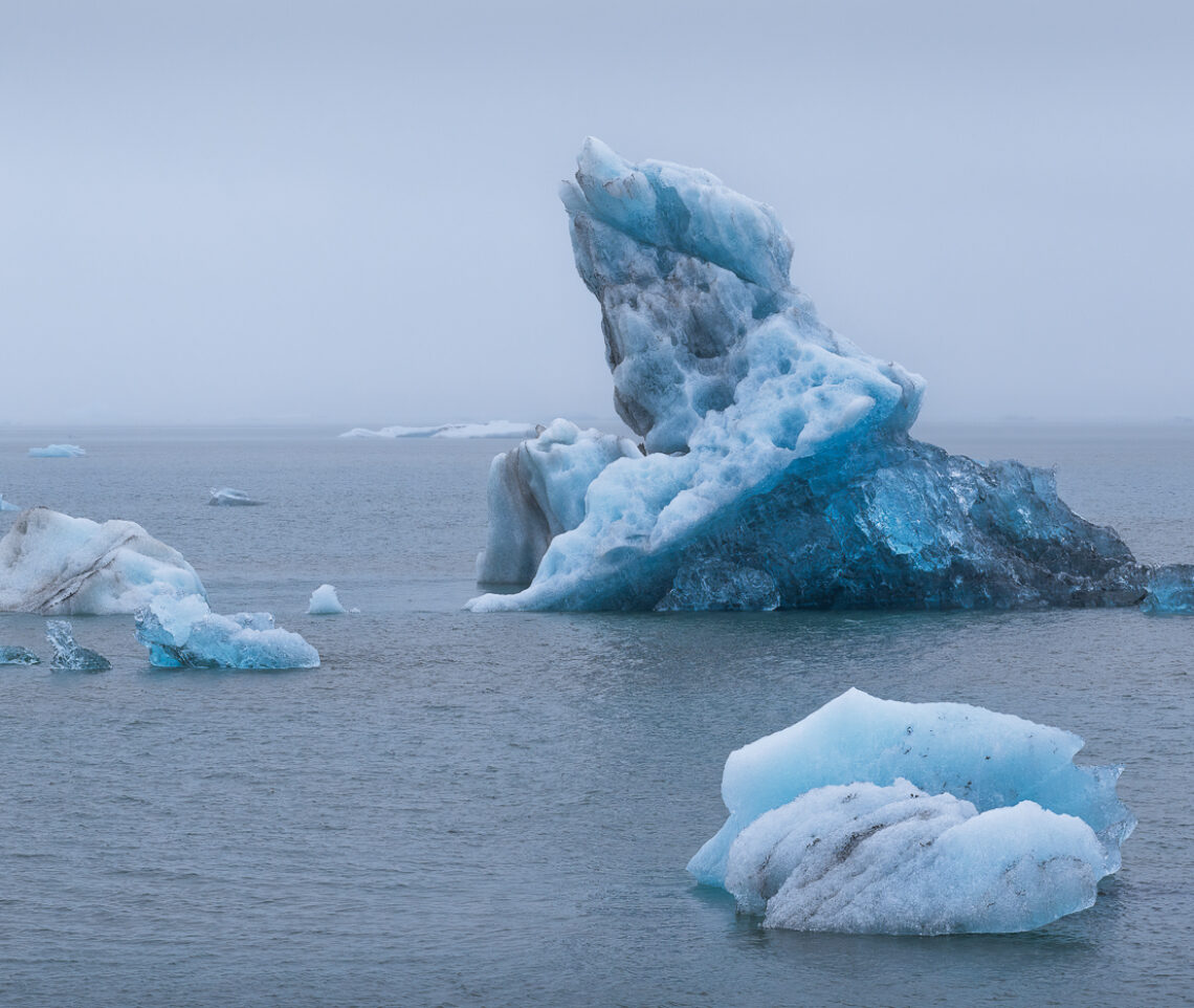 Nella nebbia, sotto una fitta e sottile pioggia battente, si palesano, nel più totale silenzio, enormi blocchi di ghiaccio galleggianti. Vatnajökull National Park, Islanda.