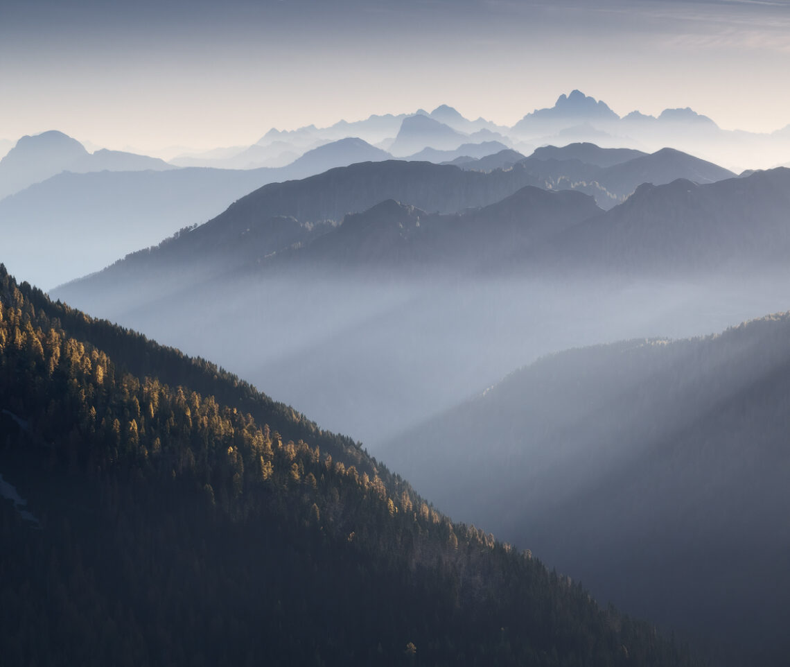 Il paesaggio delle Alpi friulane si manifesta in una sequenza di livelli modellati dalla luce del Sole. I larici gialli, però, non vogliono passare inosservati. Alpi Carniche e Giulie, Italia.