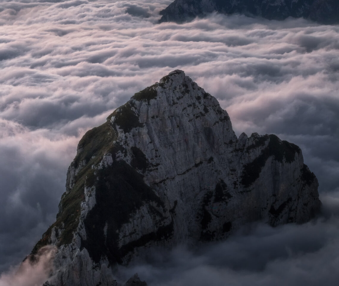 Arcipelaghi rocciosi emergono da un oceano di nubi, rivelando la via. Alpi Giulie, Carniche e Dolomiti, Italia.